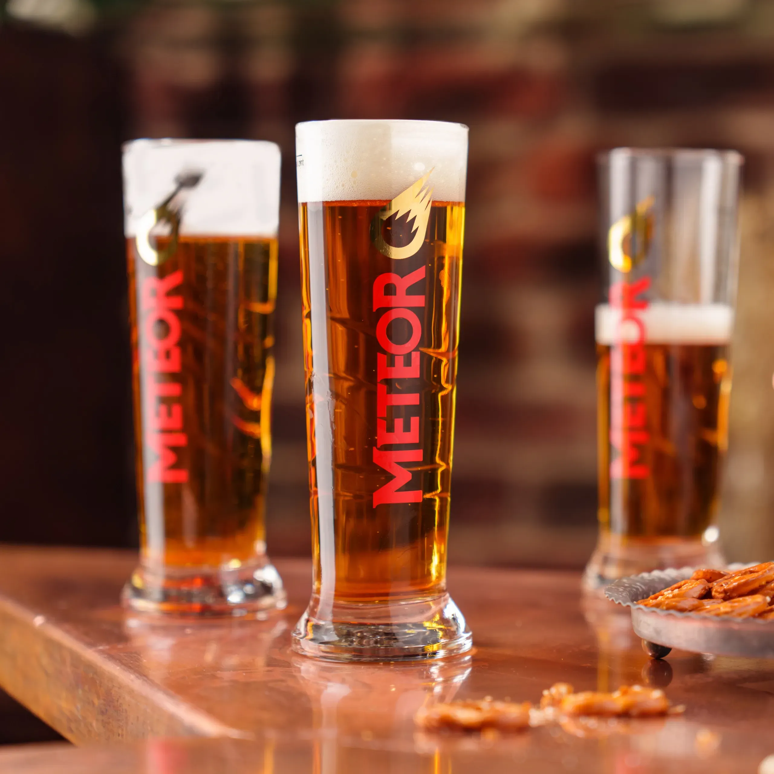 Trois verres de bière Meteor sur un comptoir en bois, photo de campagne réalisée pour la brasserie partenaire de Divinemenciel.