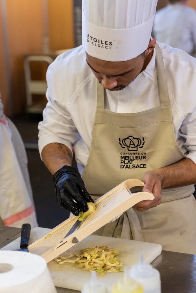 Jeune chef participant au concours du Meilleur Plat d’Alsace, épluchant des légumes pendant l’épreuve.