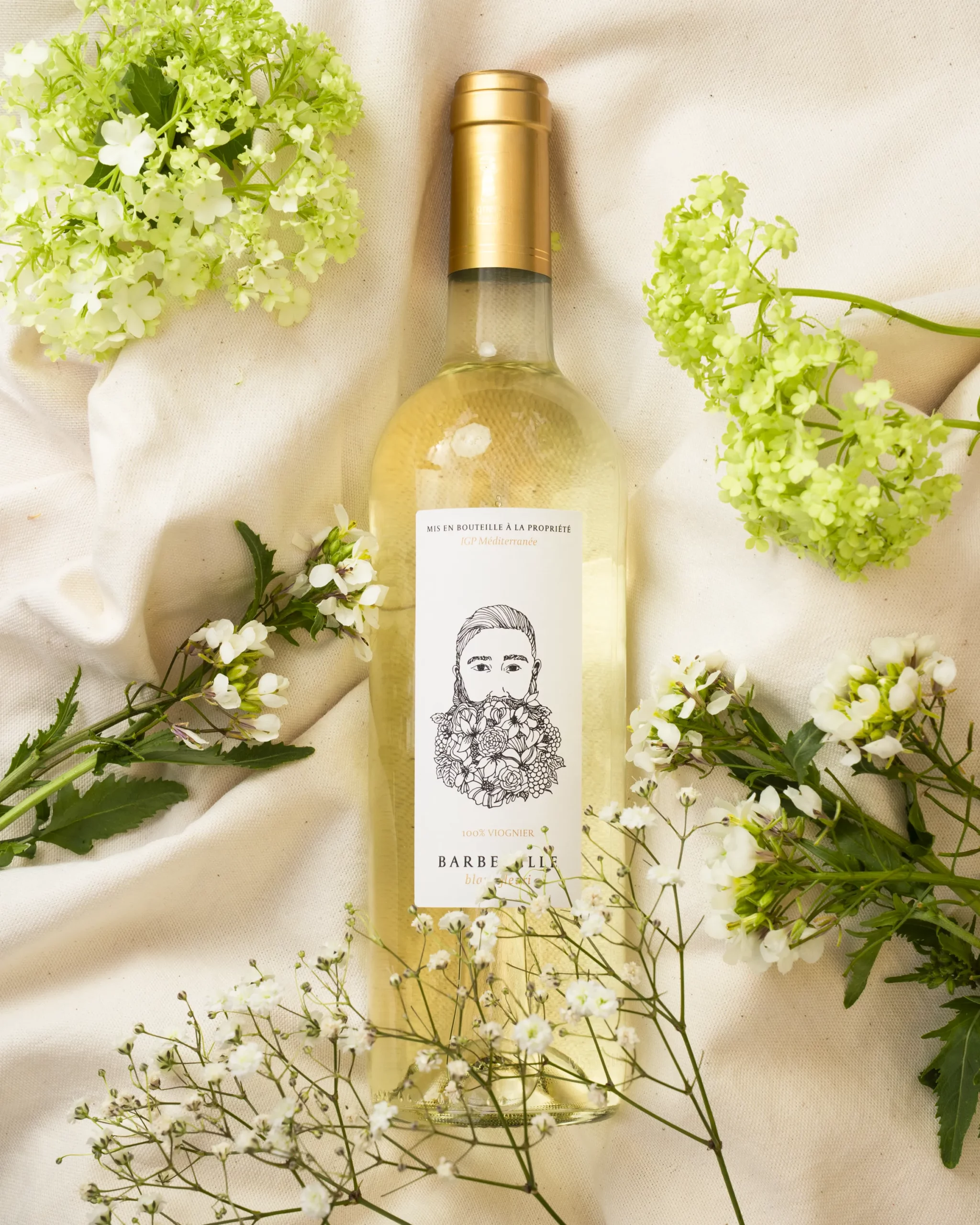 Vin blanc Vins Fleuris du Château Barbebelle entouré de fleurs blanches dans une mise en scène printanière